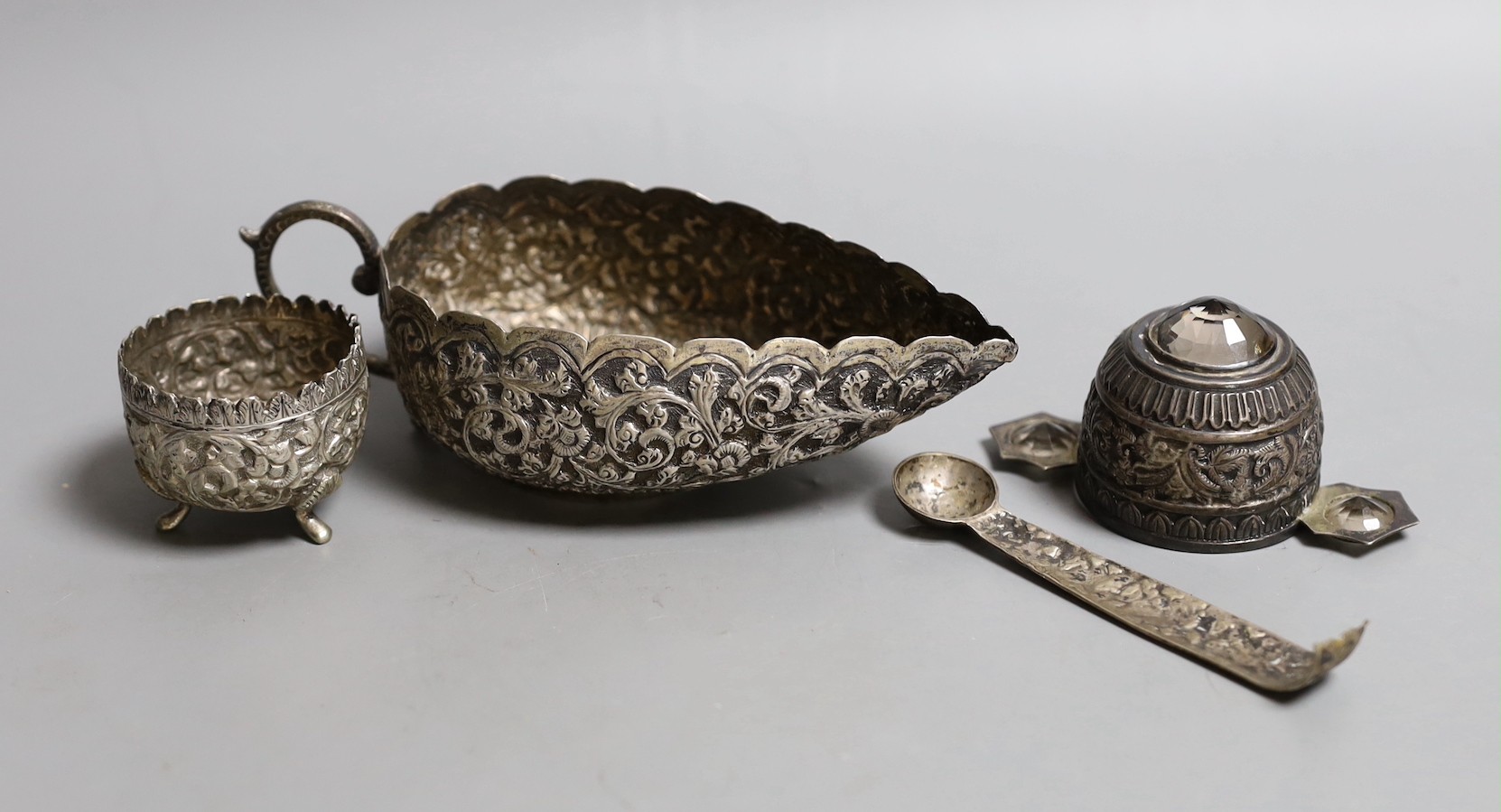 An Indian white metal gem set tasting cup, diameter 87mm, a sauce boat, salt and part of a pair of tongs (a.f.).